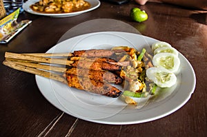 Indonesian dish Lombok: Sate Pusut marinated meat mix on stick on table with other dishes in background