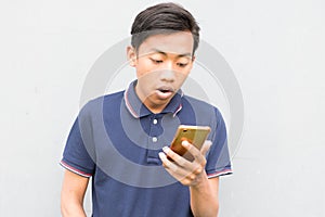 Indonesian guy with a blue t-shirt holding a smartphone and looking at it with a surprised face