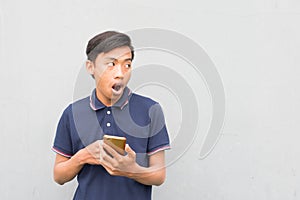 Indonesian guy with a blue t-shirt holding a smartphone and looking at it with a surprised face