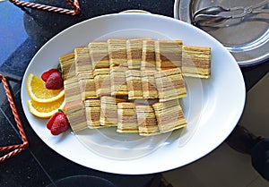 Indonesian kueh lapis served on a white plate with cut fruits on side