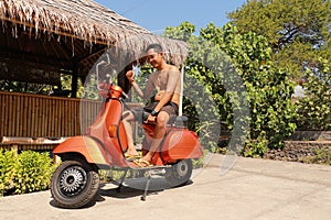 Indonesian man sitting on traditional italian scooter.Orange old-fashioned motorbike, indonesian traditional way of transportation