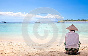 Indonesian man with straw hat sitting on the beach