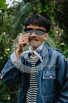 an Indonesian man in a striped shirt and denim jacket posing dashingly in a forest photo