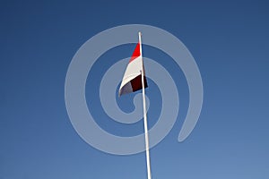 Indonesian national flag (red and white) flying against a blue sky background.