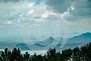 Indonesian valley scenery of forest, lake, hills, city at a distance, and thick clouds on a cloudy day