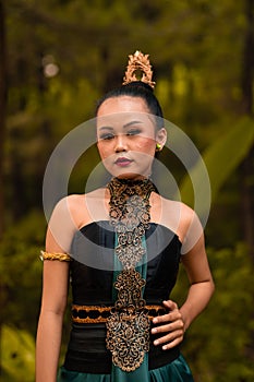 Indonesian woman with the green dress and make-up on her face standing in front of the jungle