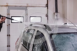 Indoor car washing. Process of removing soap foam from roof of vehicle - close-up vith selective focus.