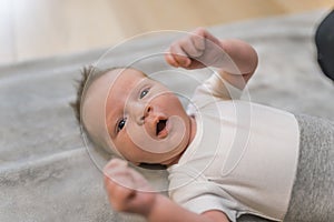 Indoor closeup portrait of a little infant baby boy clenching his fists and yawning with open mouth and eyes. Dark thin