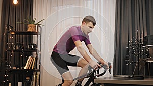 Indoor cycling. Professional cyclist in cycling apparel is riding stationary bicycle. Man is cycling on smart trainer, working out