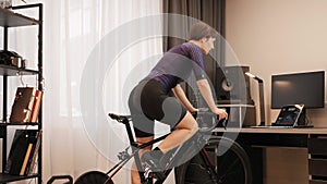 Indoor cycling. Woman is pedaling out of saddle, doing hard cycling intervals on stationary bicycle. Female cyclist is training on