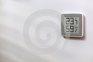 Indoor digital thermometer on white wall showing temperature, humidity level