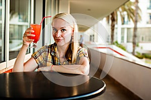 Indoor lifestyle fashion portrait of beautiful woman posing at cafe, drinking fresh healthy non-alcoholic cocktail, smiling, have