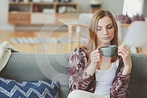 indoor lifestyle portrait of young woman relaxing at home with cup of hot tea or coffee