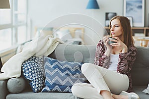 indoor lifestyle portrait of young woman relaxing at home with cup of hot tea or coffee