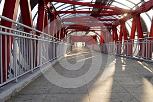 Indoor overhead pedestrian crossing with iron construction and glass ceiling. Red with tiled floor in the tunnel