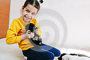 Indoor photo of happy child playing at home with little black dog. Pretty little girl with the puppy. Adorable kid playing with