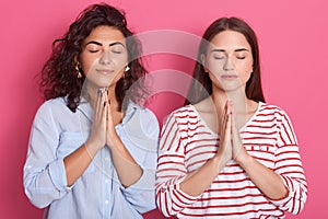 Indoor photo of serious woman have faithful expressions, keep palms pressed together, praying for good luck, females dresses