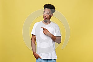 Indoor photo of young African American man pictured isolated on grey background pointing to his white blank T-shirt