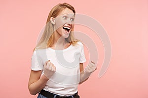 Indoor photo of young lovely woman with loose foxy hair raising excitedly her hands while screaming happily with wide mouth opened