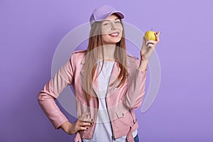 Indoor portrait of beautiful lovely teenager raising hand, holding apple, eating vitamins, being vegetarian, leading healthy