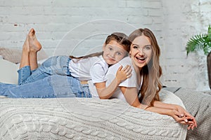 Indoor portrait of a beautiful mother with her charming little daughter posing against bedroom interior.