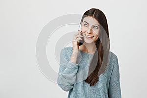 Indoor portrait of cute young female dentist, talking to her colleague via cell phone and looking aside, being in good