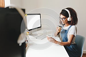 Indoor portrait of cute young woman with short hairstyle working in office with computer. Smiling black girl in
