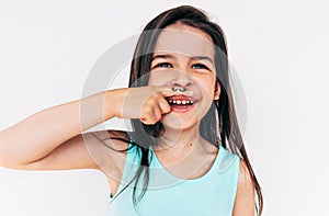 Indoor portrait of funny little girl grimacing and smiling broadly with mustache drawing on her index finger put it under the nose