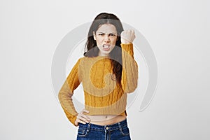 Indoor portrait of furious woman showing raised fist, grinning at camera with threatening look, frowning while standing