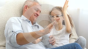 Indoor portrait of grey-haired father and little blonde girl playing with each other at home, father's day concept.