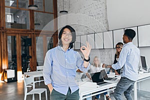 Indoor portrait of happy asian guy in stylish shirt and african tall man on background. Smiling chinese manager in