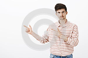 Indoor portrait of serious jealous boyfriend with beard and moustache, pointing left with finger gun gestures and