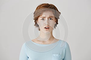 Indoor portrait of upset and disappointed young redhead female student with freckles, frowning and opening mouth in