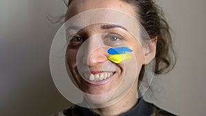 Indoor portrait of young girl with blue and yellow ukrainian flag on her cheek wearing military uniform, mandatory