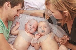 indoor portrait of young happy smiling mother and father with twin babies at home