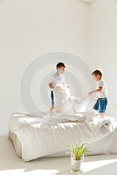 Indoor positive activity. Small children jumping on a bed and having fun fighting with pillows in sunshine