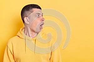 Indoor shot of astonished shocked young adult man wearing casual style hoodie, looking aside with open mouth at copy space for