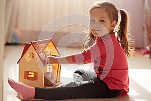 Indoor shot of baby girl playing with doll housewhile sitting at home during coronavirus quarantine, child sitting on floor and