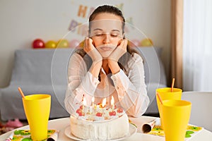 Indoor shot of bored sad Caucasian young adult woman sitting at table and looking at birthday cake, being upset to celebrate alone
