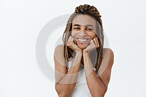 Indoor shot of carefree delighted dark-skinned girlfriend with dreadlocks and braces smiling joyfully leaning head on