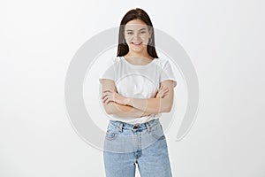 Indoor shot of carefree happy girlfriend with dark hair in stylish outfit, holding hands crossed and posing in self