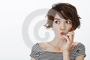 Indoor shot of curious emotive young female student with cute messy hairstyle, folding lips and saying wow while holding