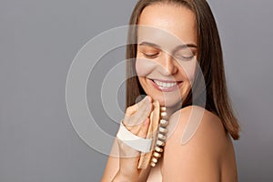 Indoor shot of cute calm beautiful woman with brown hair, massaging her body, want to have soft skin, smiling happily, enjoying