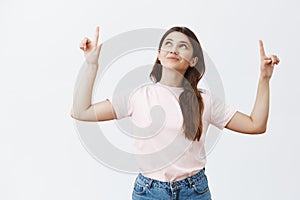 Indoor shot of cute and tender european woman wishing on star and dreaming raising index fingers pointing and looking up