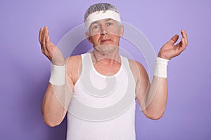 Indoor shot of elderly man shrugging shoulders and spreading hands, showing helpless gesture, posing isolated over lilac studio