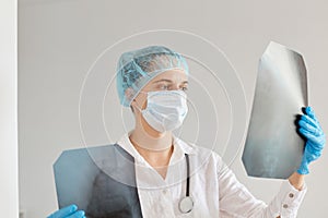 Indoor shot of female doctor looking at an x-ray, examining xray picture, woman wearing medical cap, surgical mask and gown