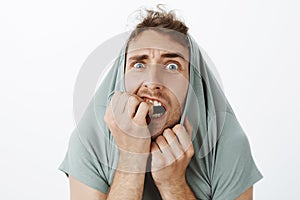 Indoor shot of funny scared caucasian guy with bristle, pulling t-shirt on head and staring with popped eyes through