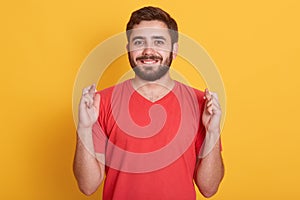 Indoor shot of glad positive bearded man crosses his fingers, anticipate hearing good news, handsome guy posing isolated over