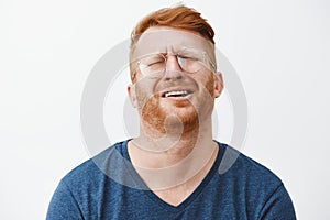 Indoor shot of gloomy and upset redhead mature man with beard, tilting head behind, frowning and grimacing, complaining