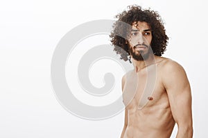 Indoor shot of handsome confident dreamy guy with curly hair and beard, looking right with focused romantic expression